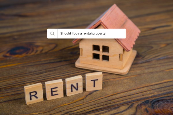 Image of tiny wooden craft house on wood table with the word "Rent" spelled out in Scrabble letters, along with an internet search box with the phrase "Should I buy a rental property"