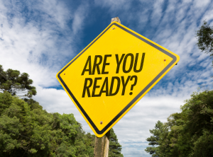 picture of yellow sign with phrase "Are You Ready?" in the middle in all capital letters. Background is a photo of a cloudy blue sky and trees.