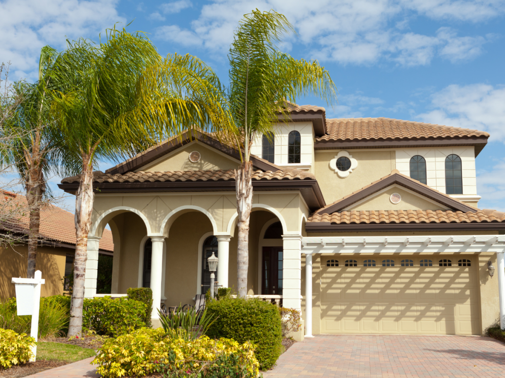 Picture of Spanish-style home front with palm trees and for sale sign in lower left